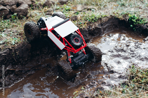 Toy rc car rising from puddle of mud. Small crawler roading on bad conditioned countryside. Bad weather, dirt racing competition of controlled toys outdoor, hero of the day, survival concept