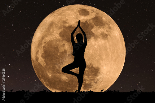 Silhouette young woman with good shape practicing yoga under full moon at night with stars photo