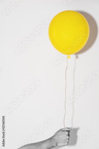 Naklejka Hand holding yellow balloon on white wall with shadow reflection