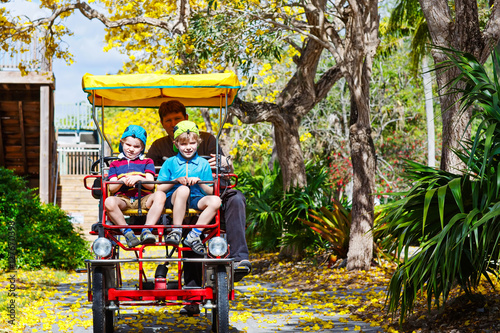 dad and two little kid boys biking on bicycle in zoo with animal photo