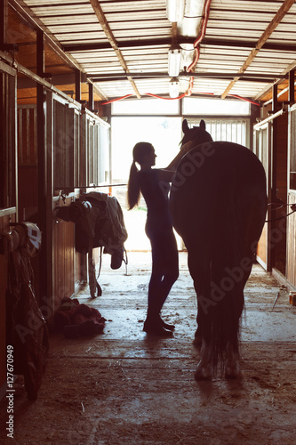 Silhouette of horsewomen owner harnessing the stallion in stable