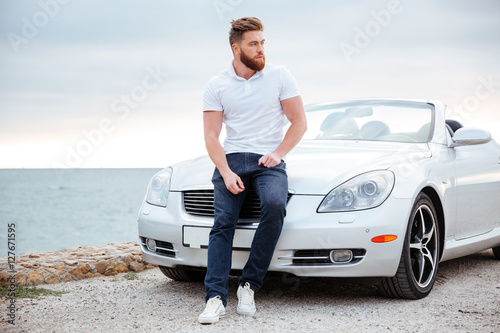 Young bearded man leaning on his car