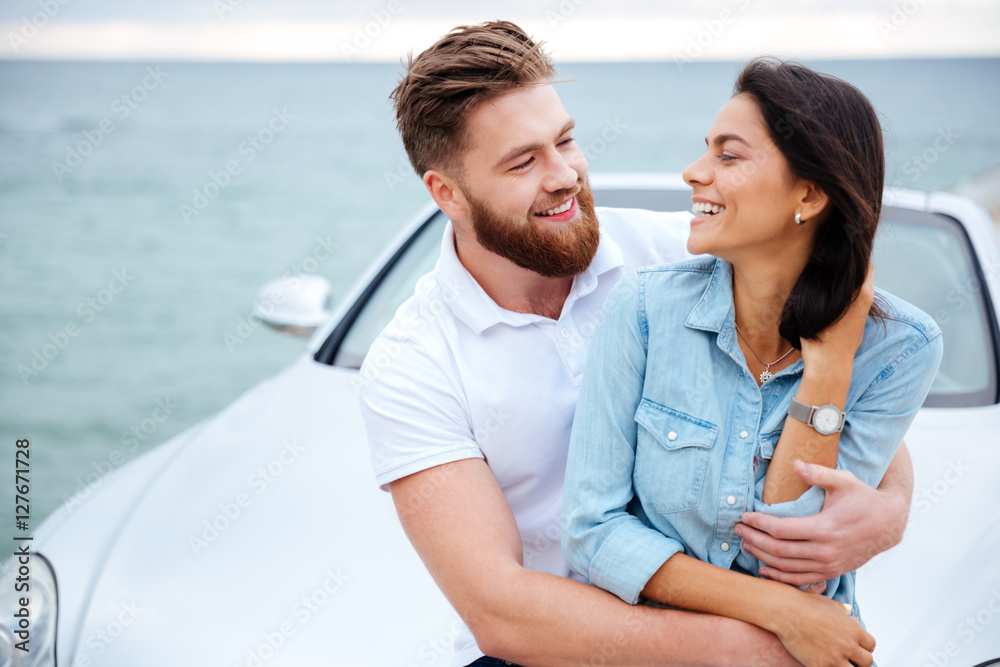 Obraz premium Young couple embracing while standing near car at the seaside
