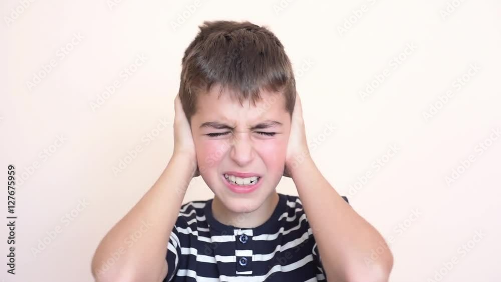 Young boy with closed eyes covering his ears with hands because of loud noise Young boy with closed eyes covering his ears with hands because of loud noise