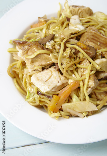 A dinner dish of chicken noodle stir fry on a blue wooden dining table background