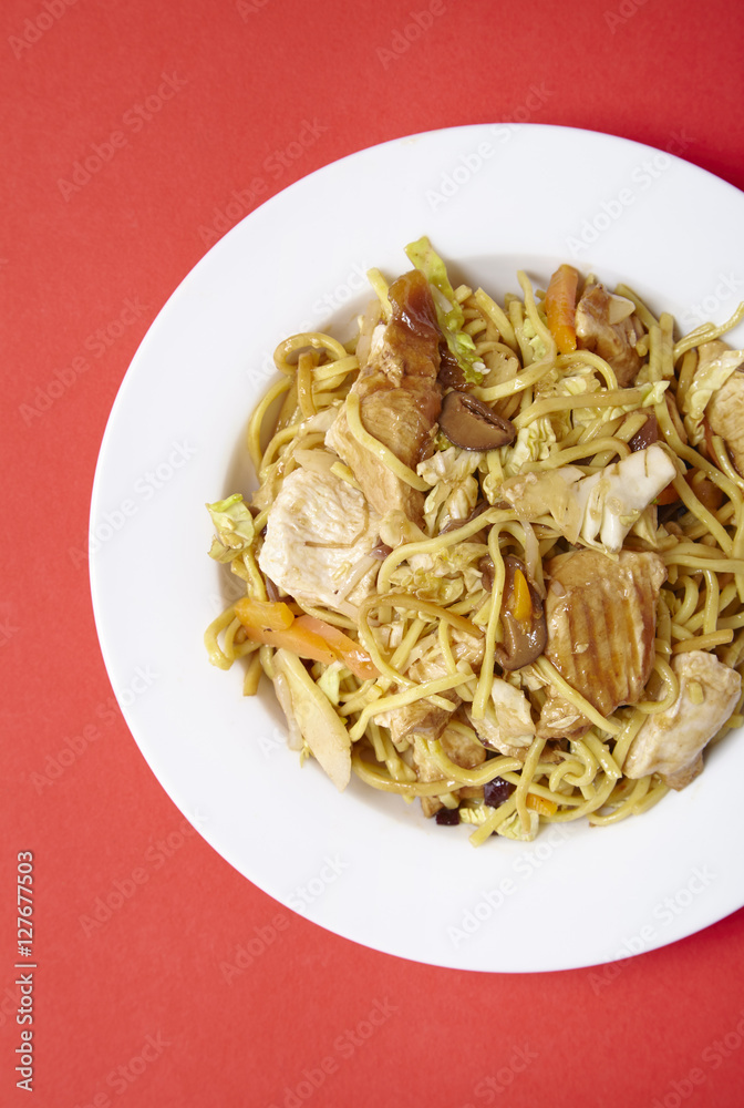 Overhead view of a dinner dish of chicken noodle stir fry on a bright red background Overhead view of a dinner dish of chicken noodle stir fry on a bright red background