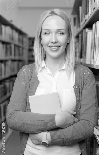 Smiling blond student  holding a book in library at the universi photo