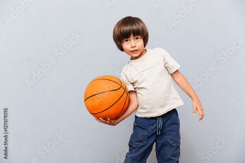 Smiling little boy standing and playing with basketball ball