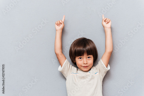 Portrait of happy little boy pointing up with both hands photo