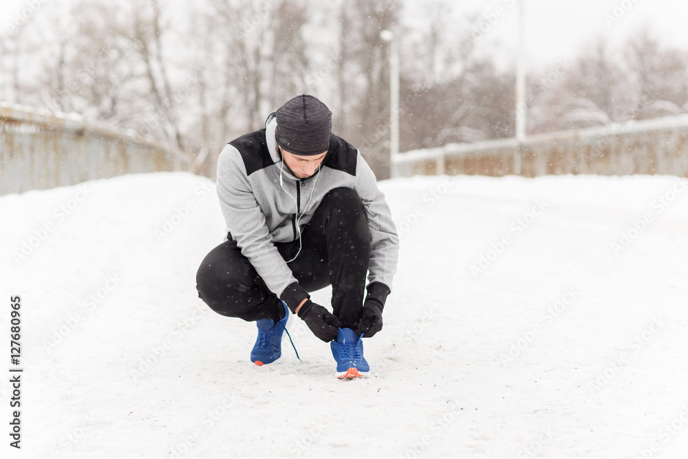 man with earphones tying sports shoe in winter