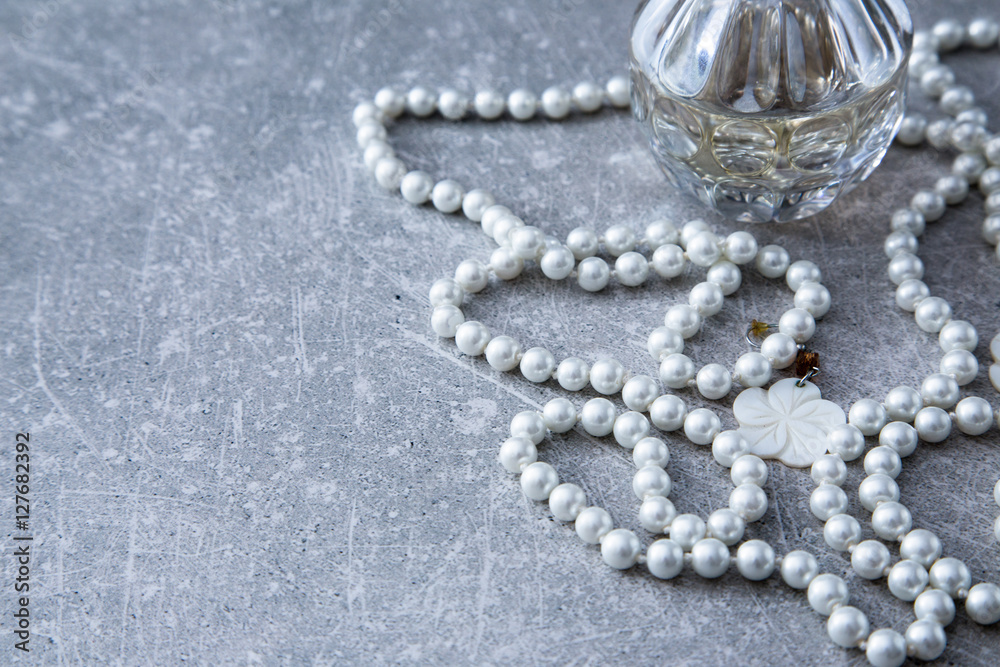 a strand of pearls and perfume on a stone background