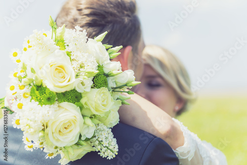 Brautpaar küsst sich mit Blumenstrauß
