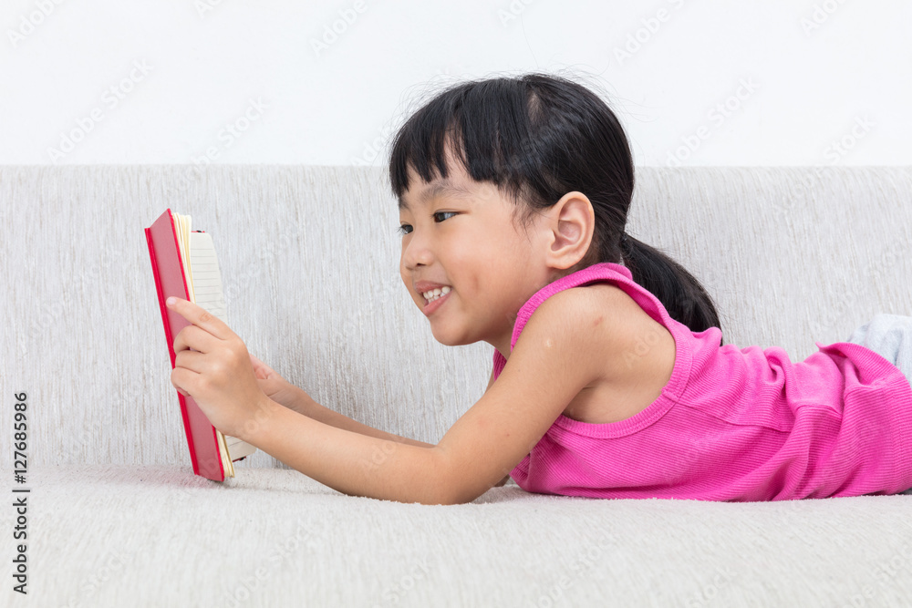 Happy Asian Chinese little girl laying on sofa with book Happy Asian Chinese little girl laying on sofa with book