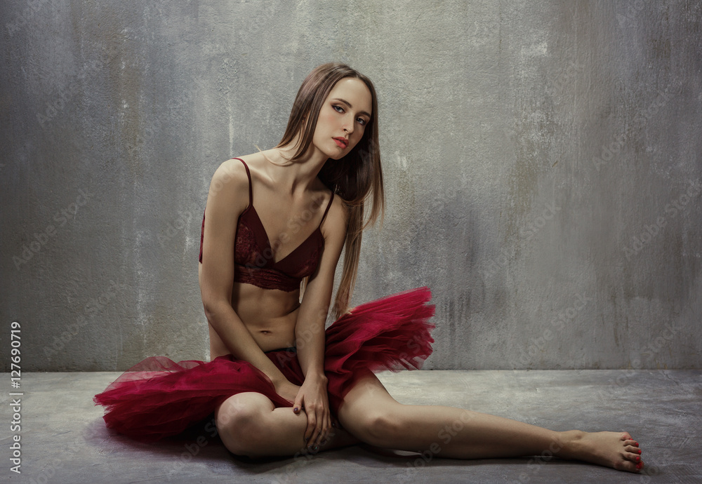 Portrait of slim young girl dancer in red tutu is sitting on a b