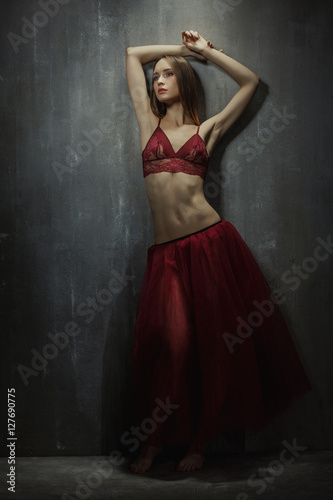Portrait of slim young girl dancer in red long skirt that sits o