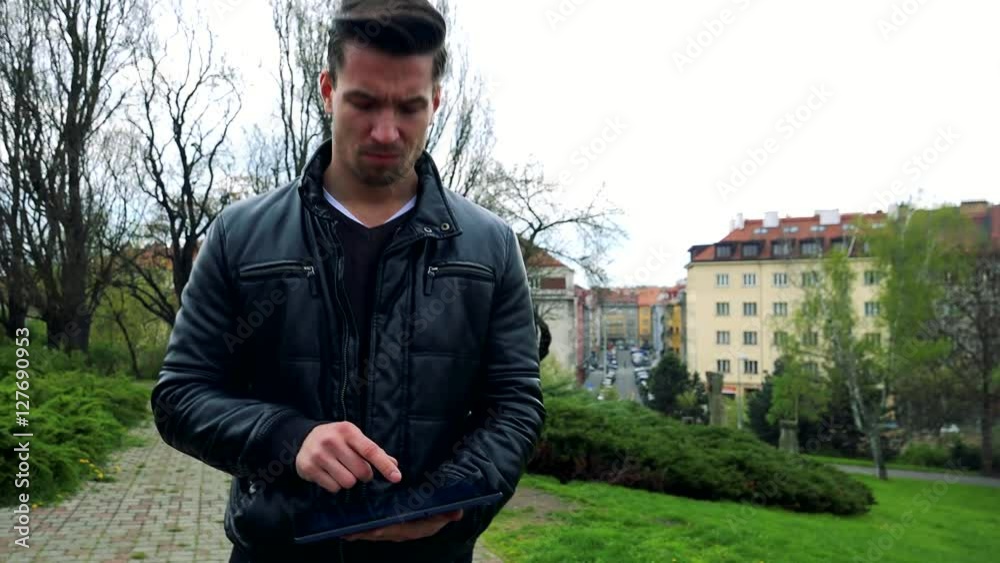 Young handsome man goes and works on tablet computer in park Young handsome man goes and works on tablet computer in park
