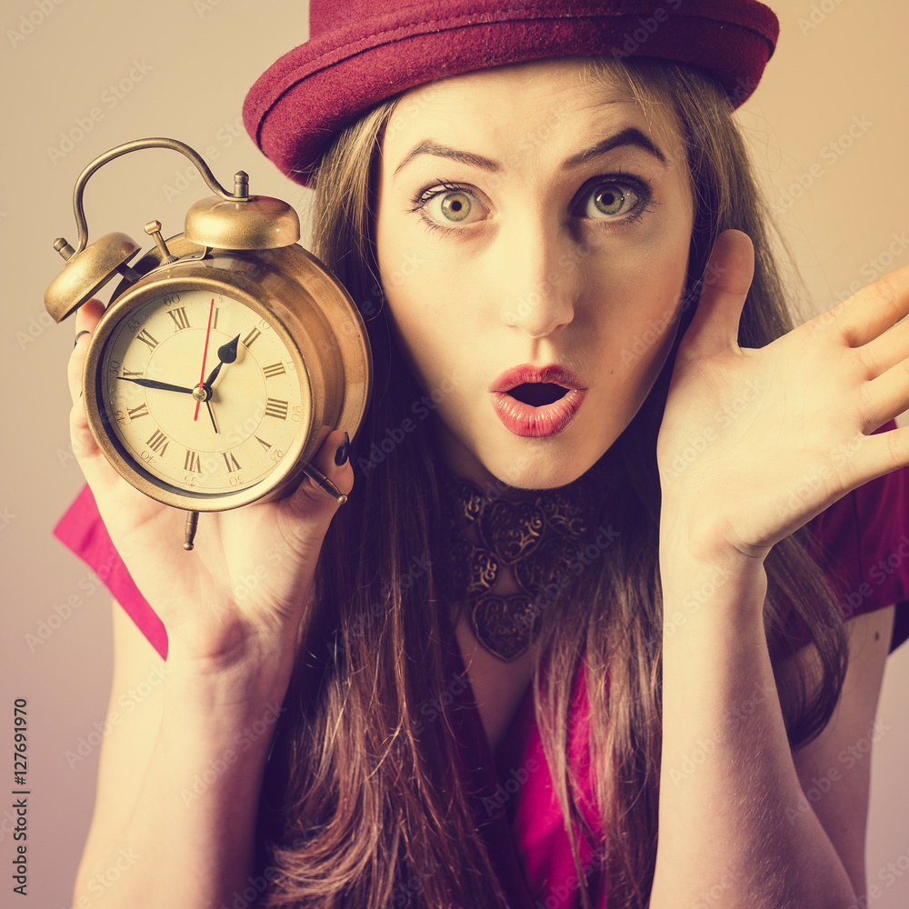 Portrait of elegant beautiful young lady in hat showing alarm clock