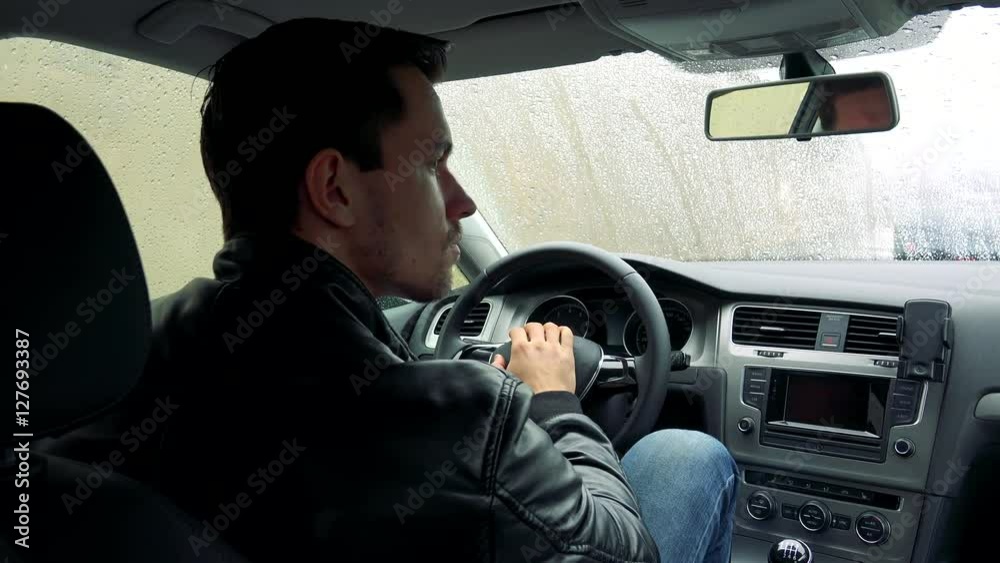Young handsome man sits in car on place for driver and observes the landscape Young handsome man sits in car on place for driver and observes the landscape