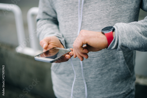 Modern sport and running concept. Urban runner using sporty smart watch and smartphone for training.