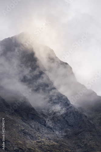 Mysterious mountain peak top covered in misty clouds golden glow by sunlight