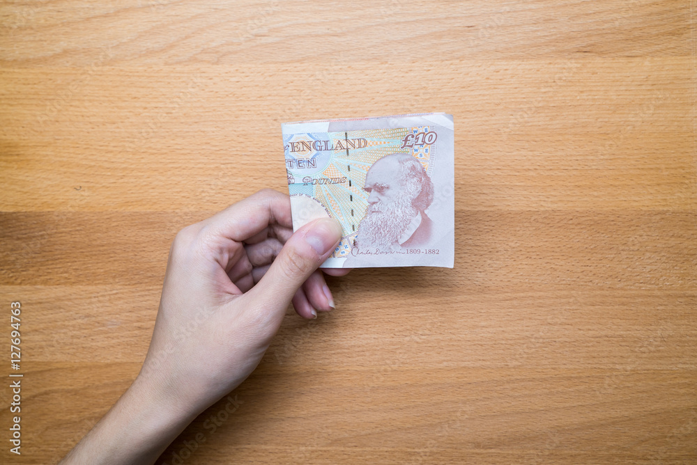 Hand giving stack of ten pound sterling English money with copy space Hand giving stack of ten pound sterling English money with copy space