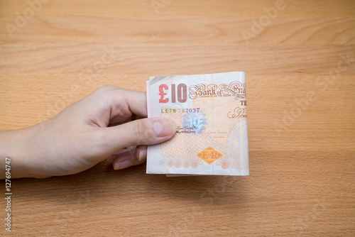 Hand giving stack of ten pound sterling English money with copy space