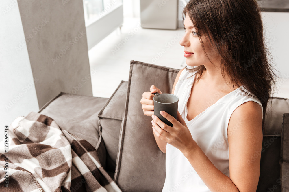 Peaceful woman sitting on sofa and drinking coffee