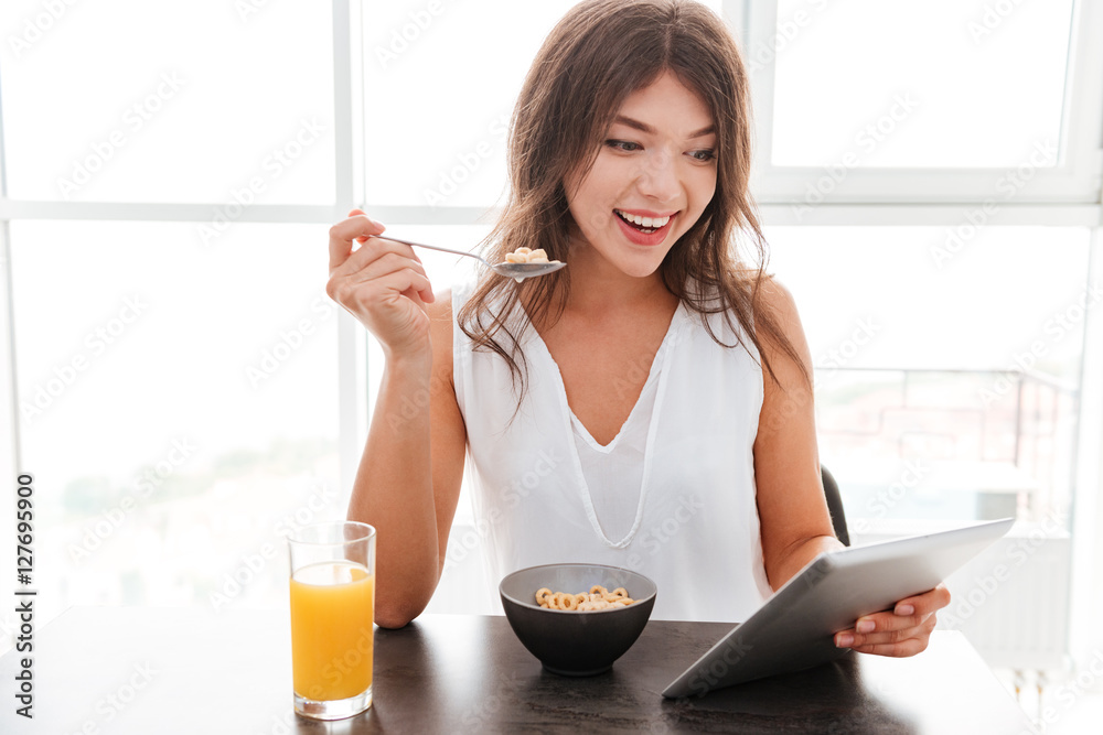 Cheerful young woman having breakfast and using mobile phone Cheerful young woman having breakfast and using mobile phone