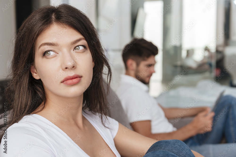 Sad woman sitting while her boyfriend using tablet at home Sad woman sitting while her boyfriend using tablet at home