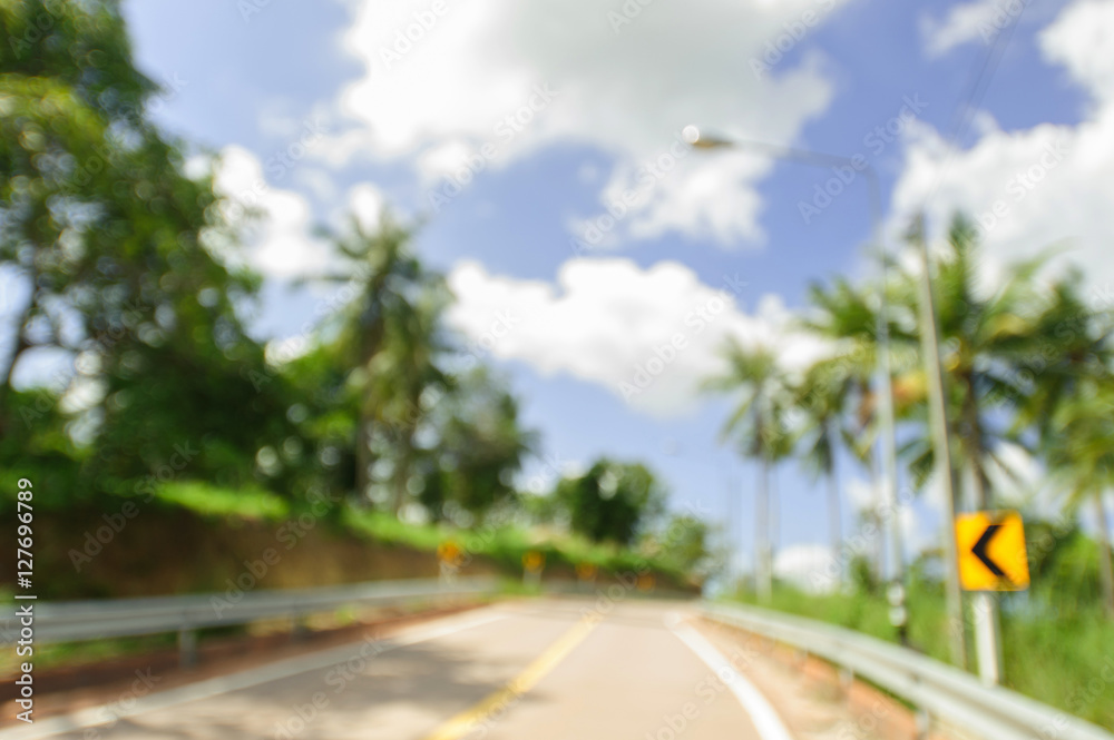 The road and coconut palm trees blurry photo background. Tropical scene defocused