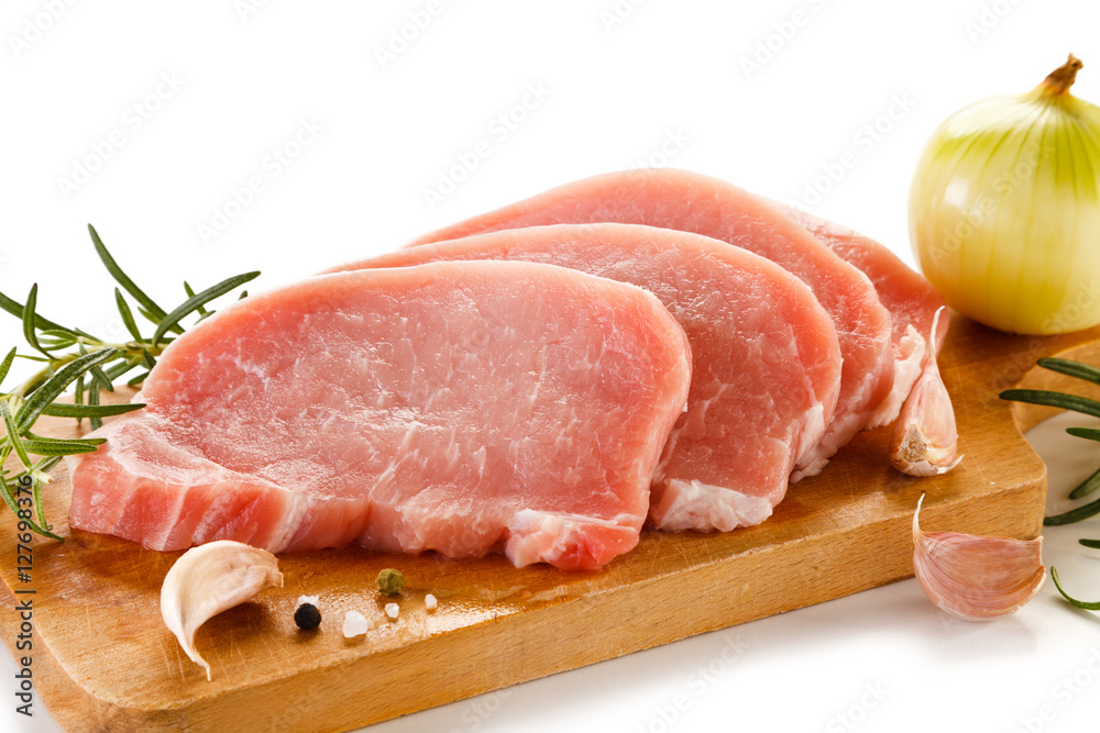 Raw pork chops on cutting board and vegetables Raw pork chops on cutting board and vegetables