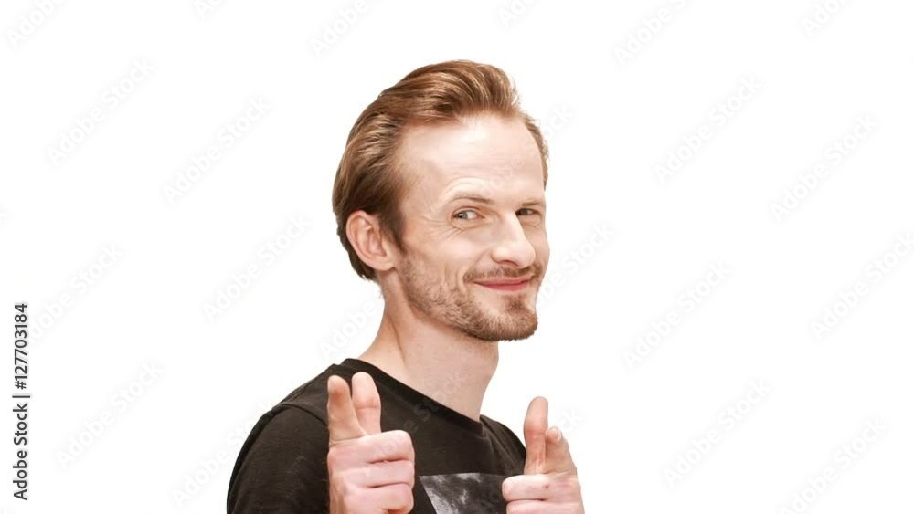 Young handsome man smiling, pointing fingers at camera, passing by over white background. Slow motion. Young handsome man smiling, pointing fingers at camera, passing by over white background. Slow motion.