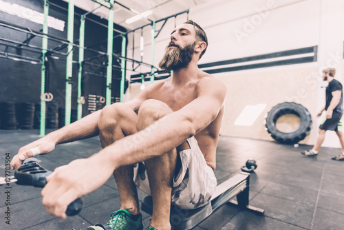 Young male cross trainer training on rowing machine in gym
