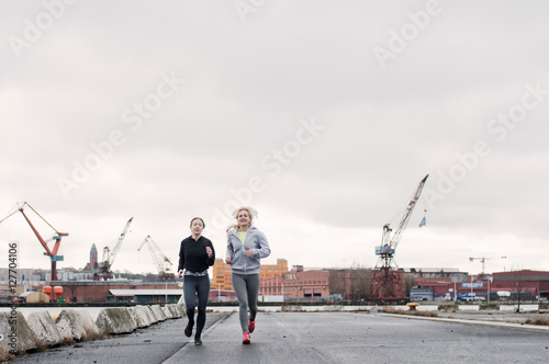 Two female running friends running along dockside