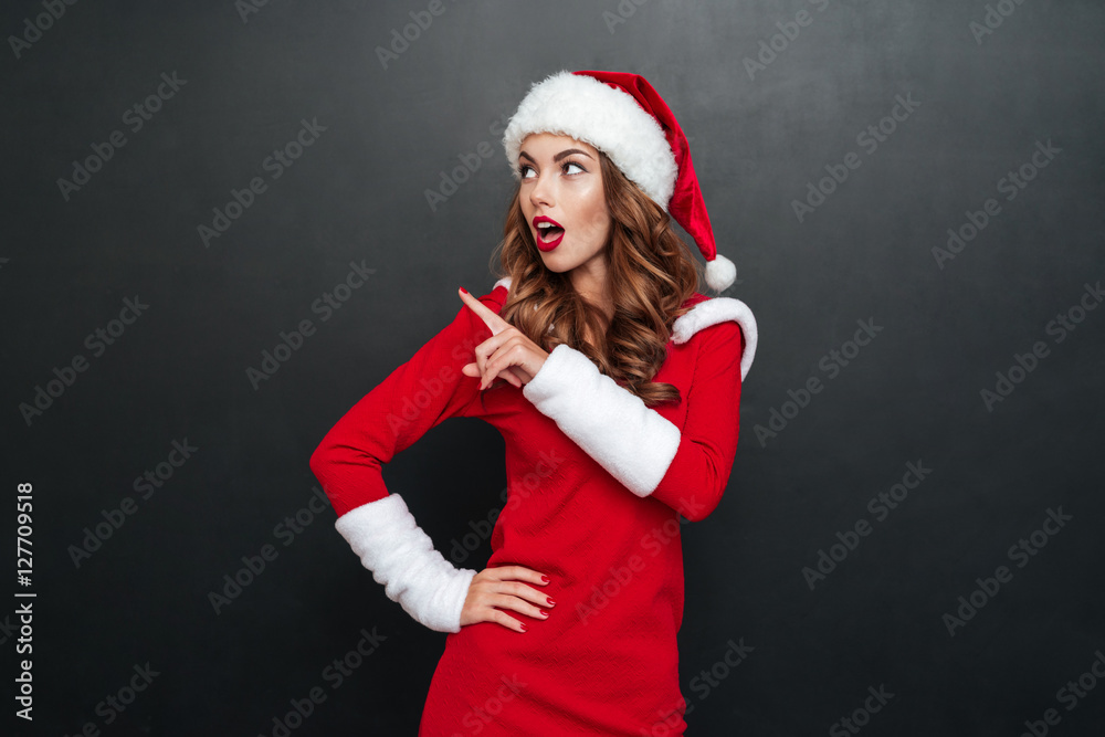 Naklejka premium Surprised woman in christmas dress with finger point aside