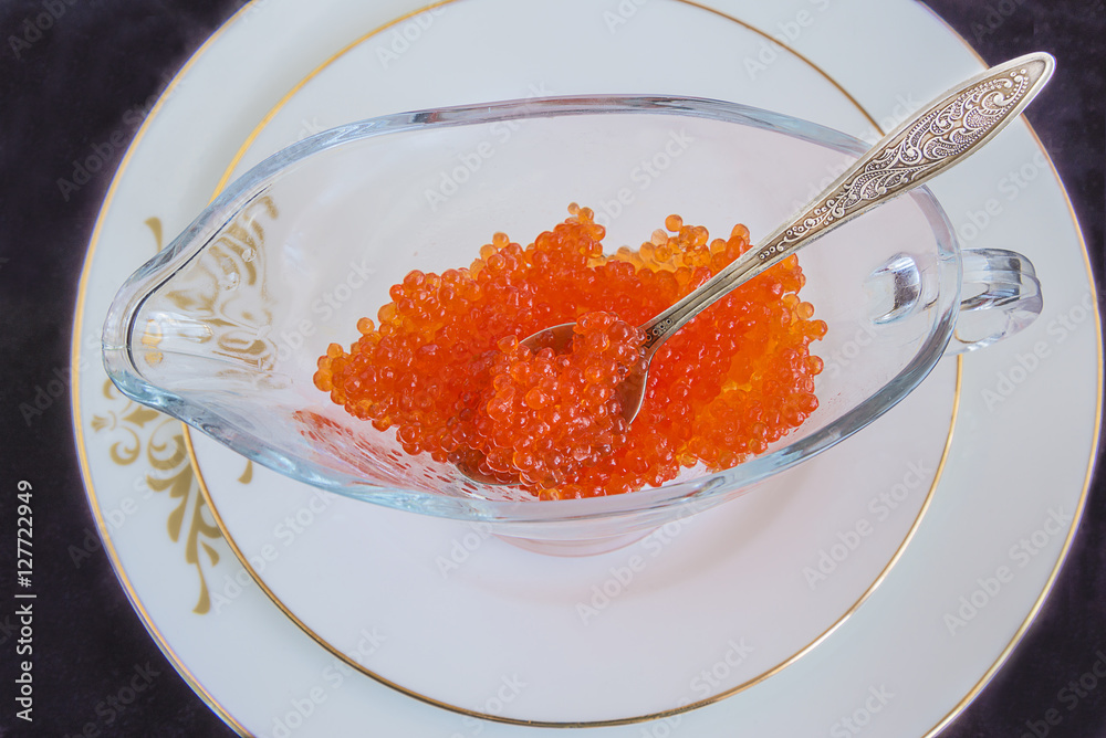 Luxurious meals: red caviar or salmon roe on white plate on black background Luxurious meals: red caviar or salmon roe on white plate on black background