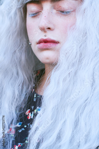 Retrato de primer plano de una adolescente extraña con el pelo blanco, piercings y los ojos cerrados photo