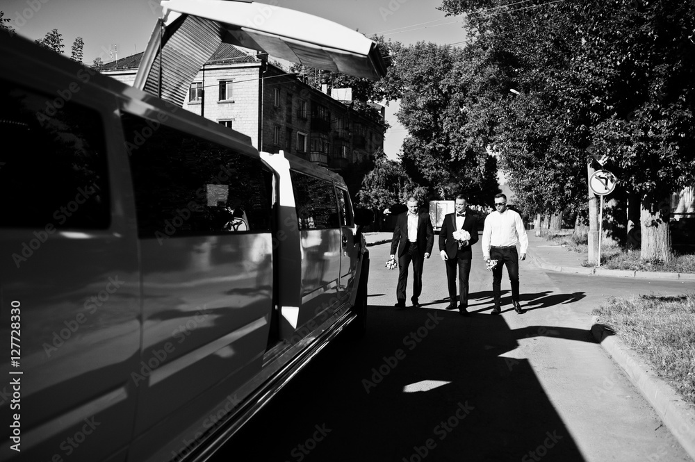 Three handsome guys walking into luxury limousine. Groom with be