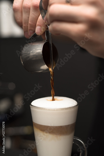 Barista is pouring coffee in milk - preparing coffe latte