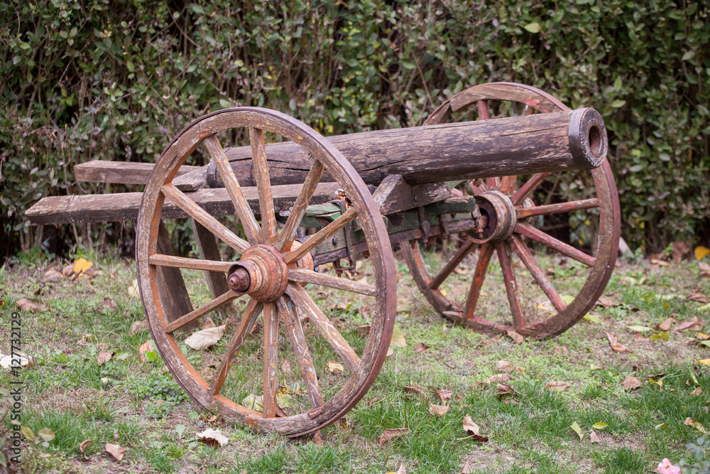 Old antique cannon with wooden wheels on grass.