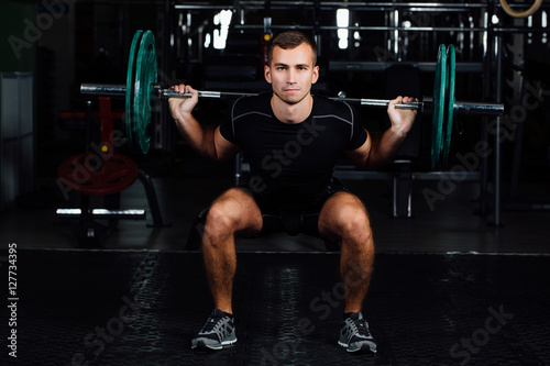 Man training squats with barbells over head.