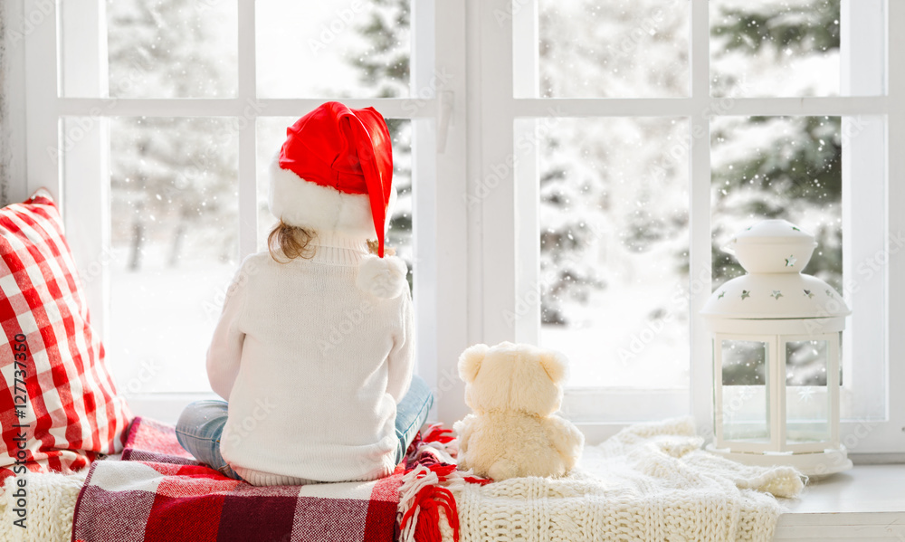 Fototapeta premium happy child girl sitting back in winter window Christmas