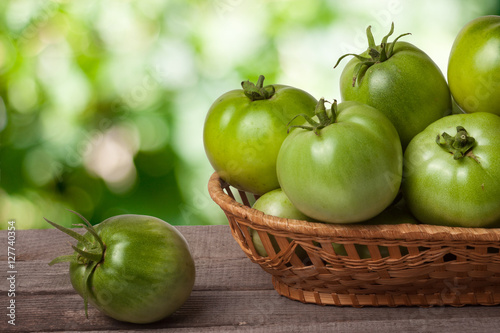 unripe green tomatoes in a wicker basket on wooden table with blurred background