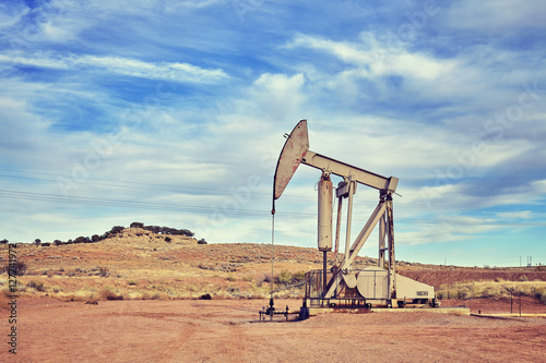 Retro toned picture of an oil pump, old industrial equipment on arid soil.