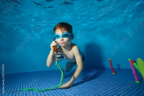 Little boy underwater swims and plays in the pool with the handset. Portrait. Shooting underwater. Landscape orientation
