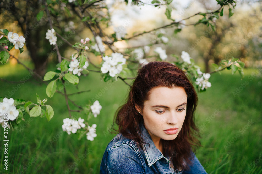 Young pretty serious caucasian woman in jeans jacket standing near blooming spring tree. Youth, freshness, beauty, happiness concept. Young pretty serious caucasian woman in jeans jacket standing near blooming spring tree. Youth, freshness, beauty, happiness concept.