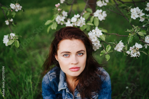 Young pretty serious caucasian woman in jeans jacket standing near blooming spring tree. Youth, freshness, beauty, happiness concept. © anna_gorbenko