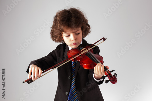 Little curly boy playing the violin. Gray background.