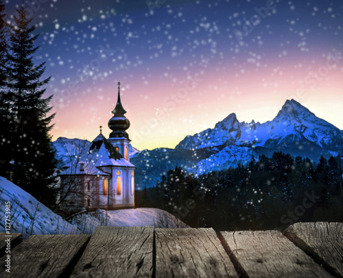 verschneite Winterlandschaft mit kleiner, beleuchteter Kirche in der Dämmerung