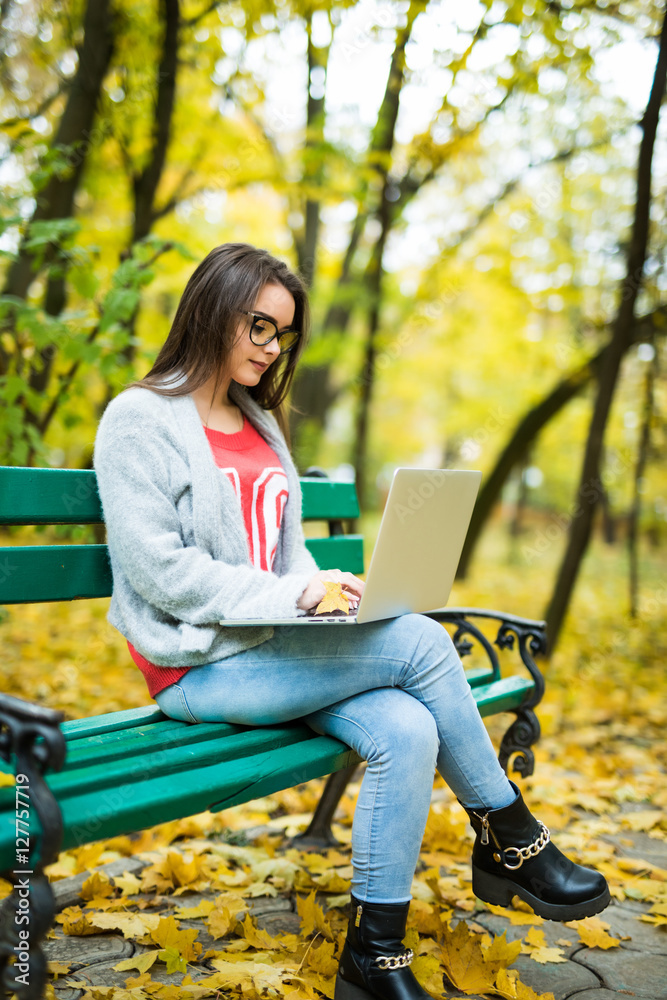 Young happy girl students working on laptop in autumn park Young happy girl students working on laptop in autumn park